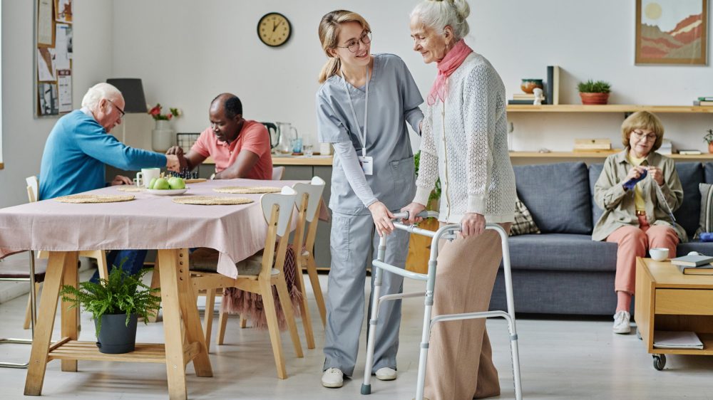 Young volunteer in uniform caring about senior people in nursing home